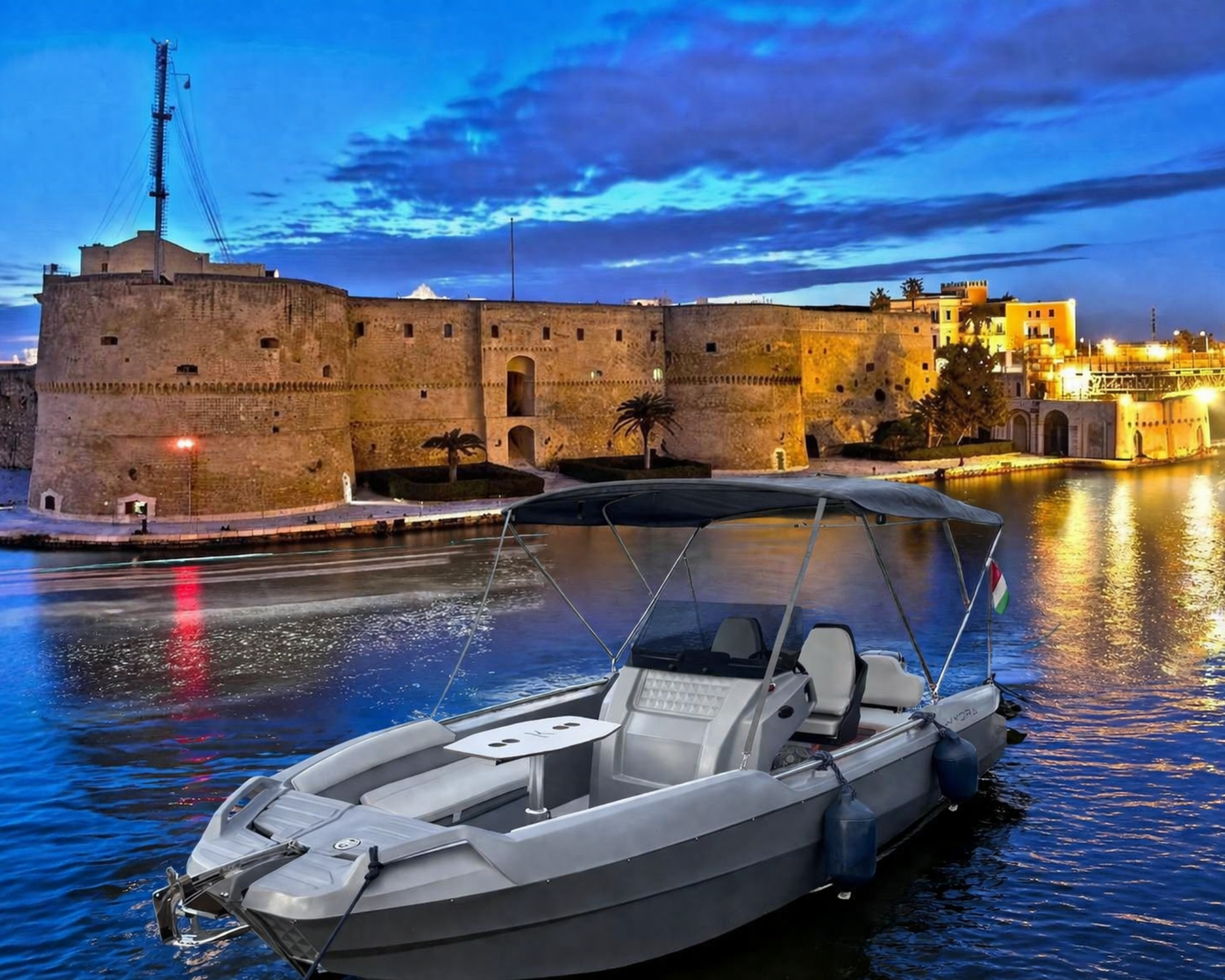 Motoscafo open grigio in porto al crepuscolo con castello illuminato sullo sfondo